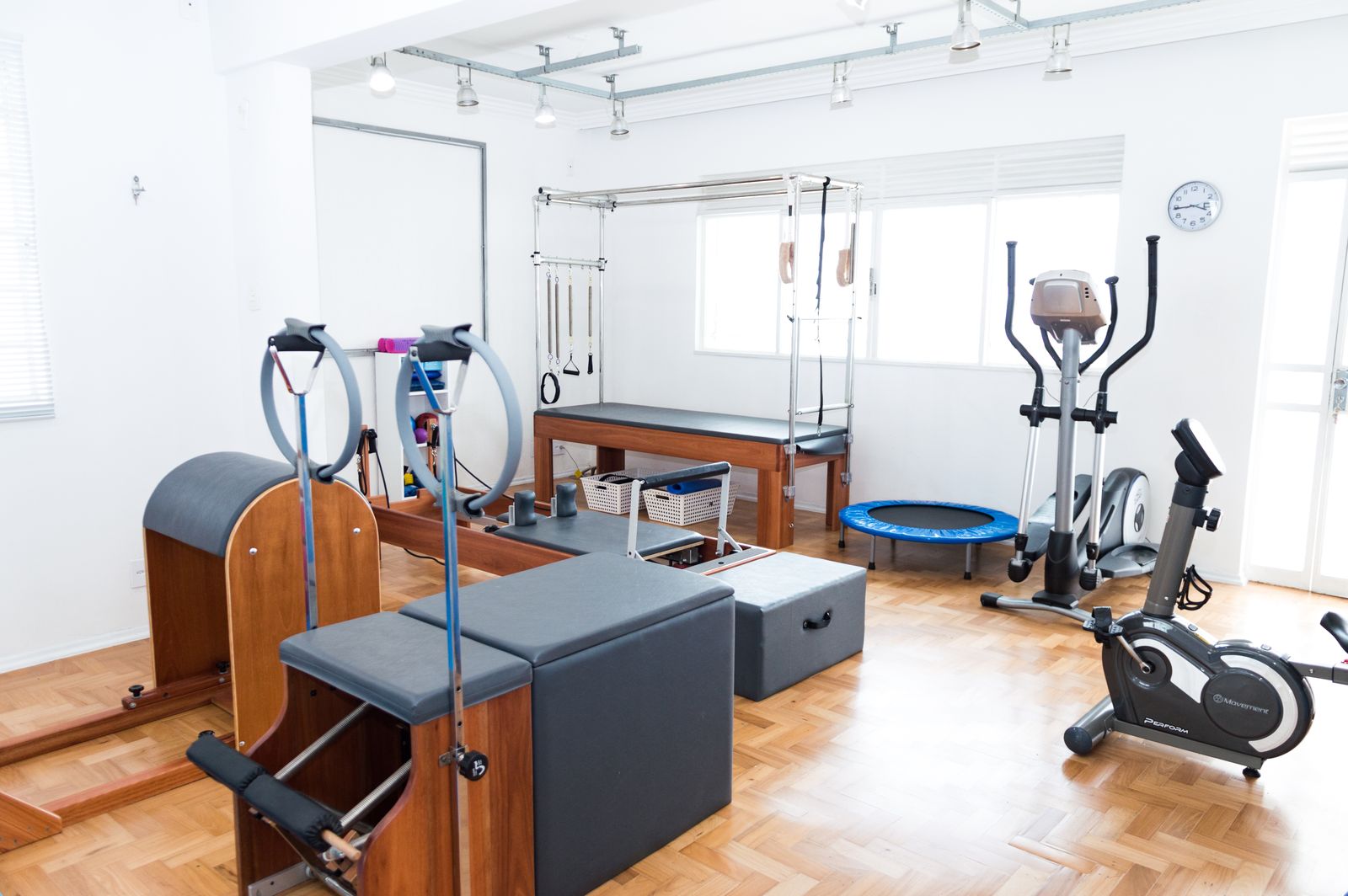 Espaço de academia iluminado com equipamentos de Pilates, bicicletas ergométricas e piso de madeira para uma experiência de treino moderna.